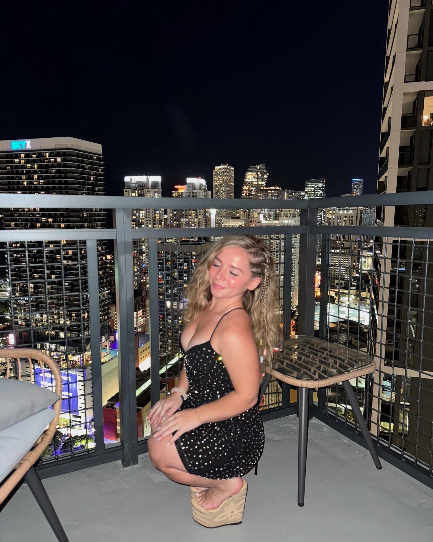 Shy Tayla in a black sequin mini dress on a rooftop with the Miami skyline behind her
