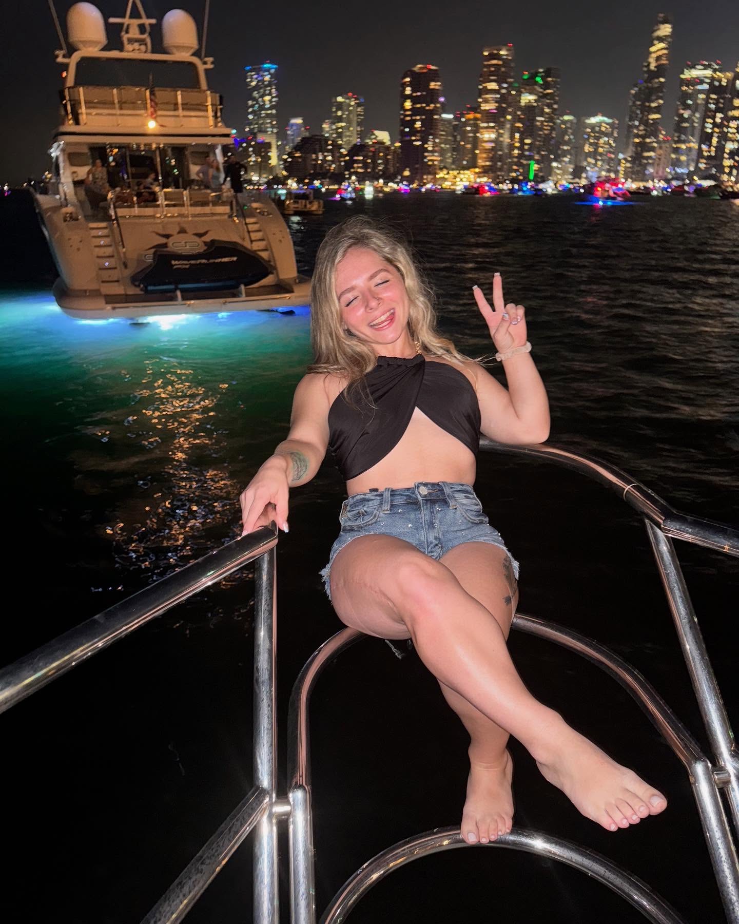 Shy Tayla on a yacht at night with the Miami skyline lit up behind her